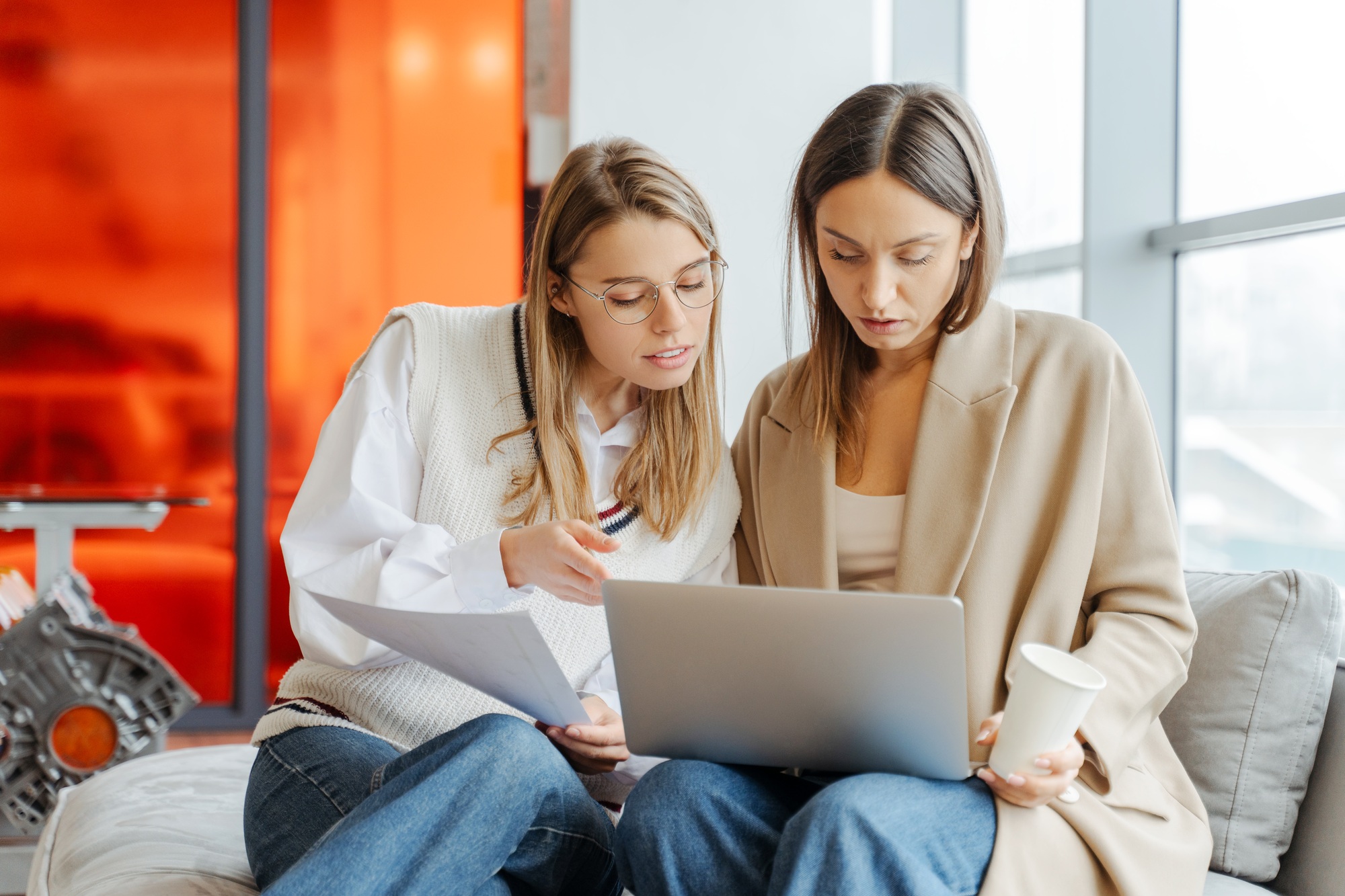 Two businesswomen working together meeting using laptop and documents in modern office
